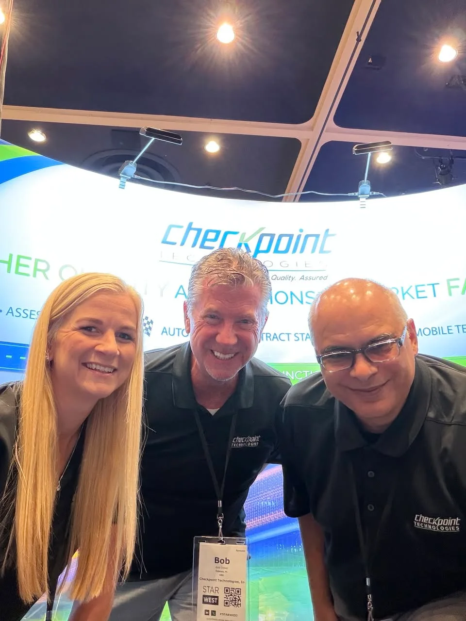 Three people taking a selfie in front of the Checkpoint Technologies display.